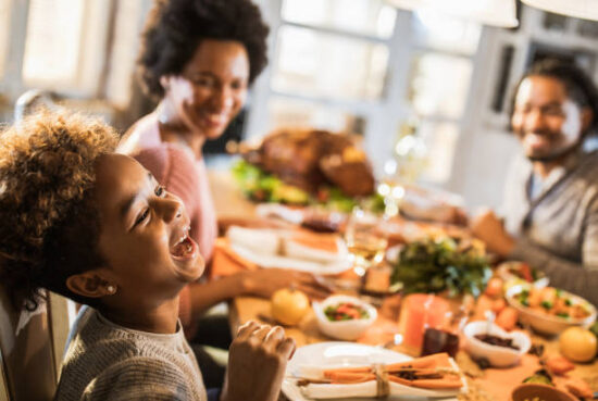 Cheerful black girl laughing while having a meal with her parents in dining room.