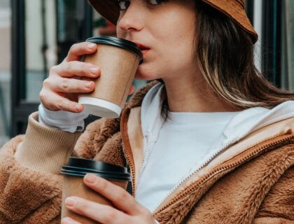 woman in brown jacket drinking two cups of coffee