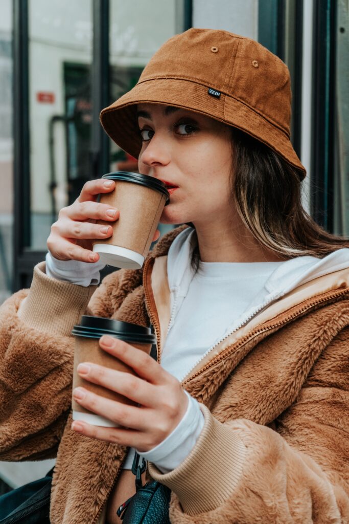 woman in brown jacket holding two paper coffee cups