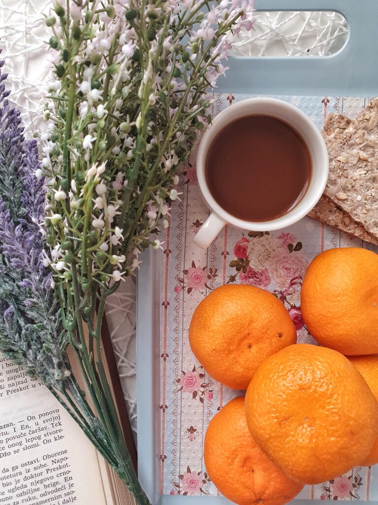 cup of coffee next to book and oranges