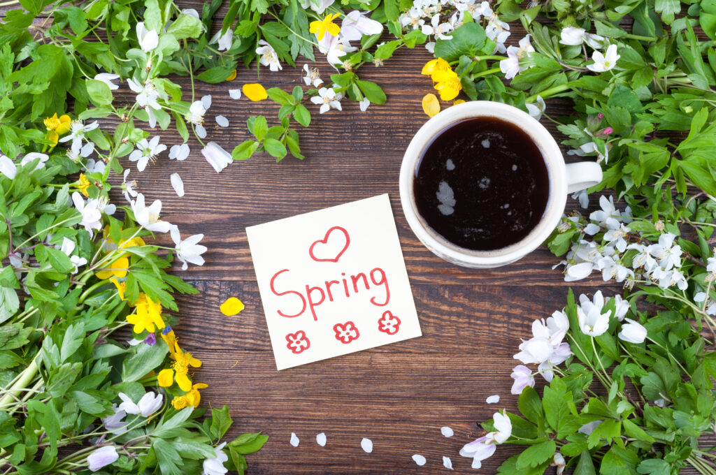 Cup of coffee on a spring background. Coffee, flowers, and a note with the word spring on a wooden surface