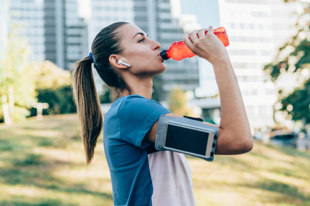 A sporty woman drinking energy supplements from bottle after exercising outdoors.