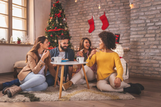 Group of young friends spending Christmas day at home together, drinking coffee, eating Christmas cookies and having fun