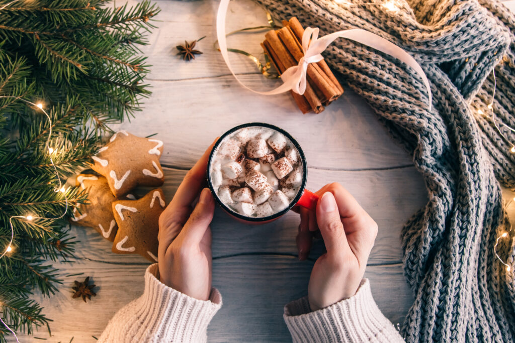 The top view of a female hands hold a cup of coffee with marshmallows during the festive season.