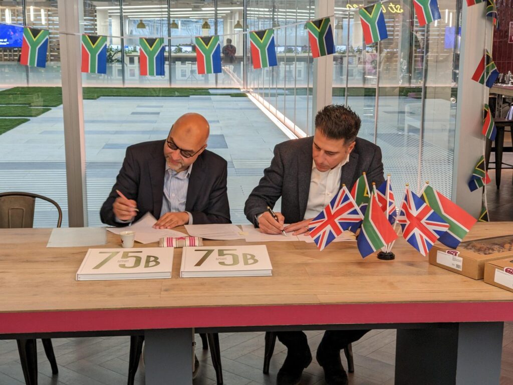 two men writing on a page with Britan and South African flags around them 