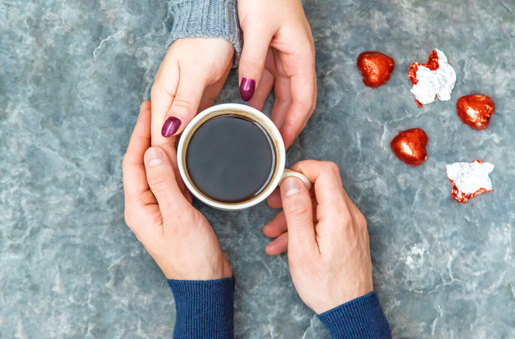 a woman and a man holding hands around a cup of coffee