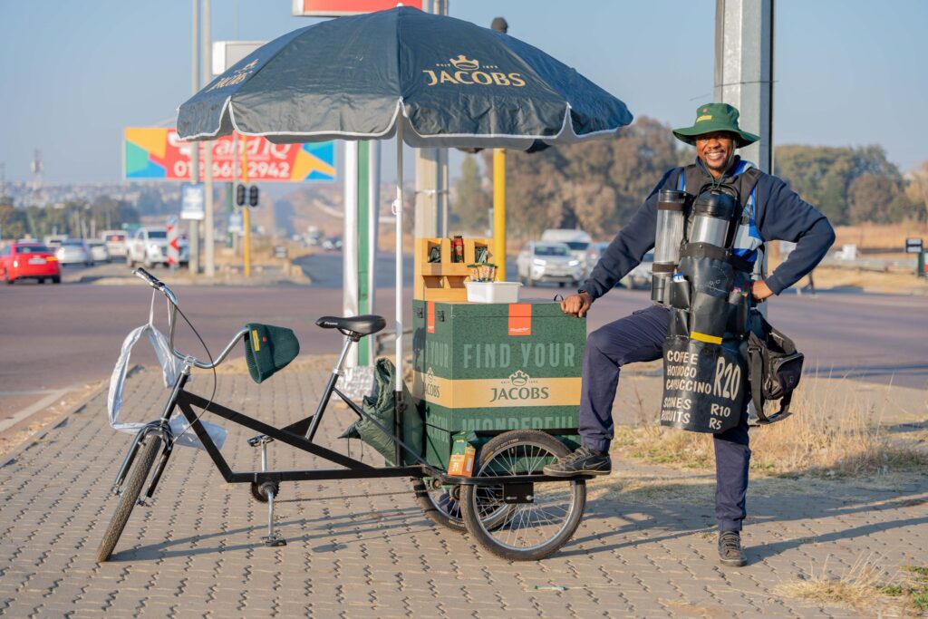 Lehubedu Mohlab standing with a bike with a jacobs coffee storage box 