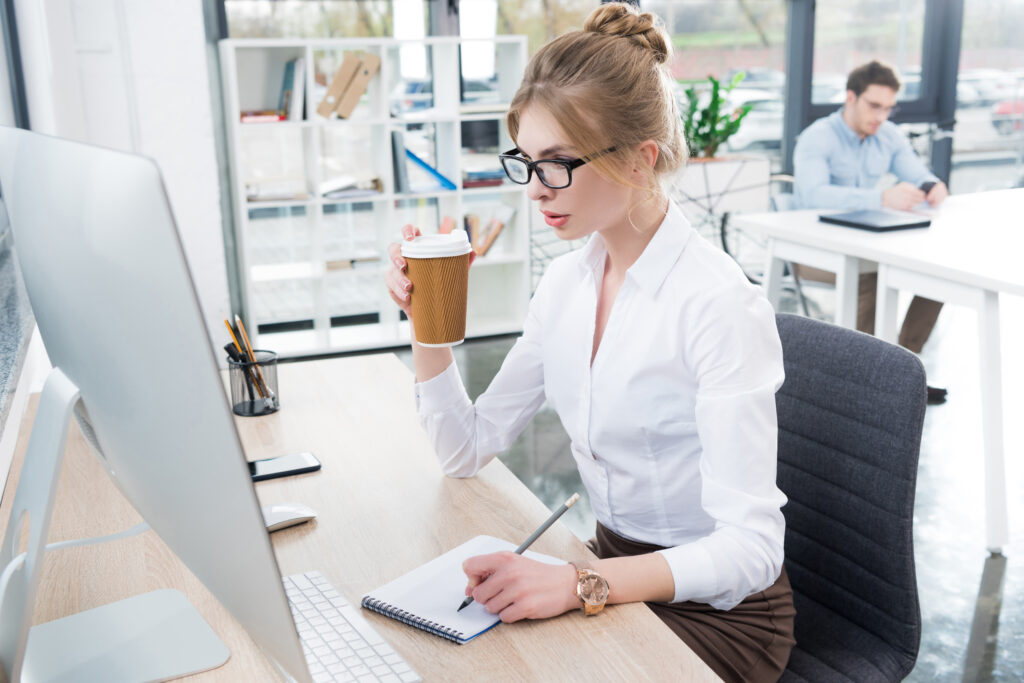 concentrated beautiful businessman drinking coffee and working with computer in modern office