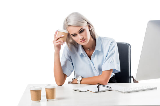 portrait of tired businesswoman at workplace with disposable cups of coffee, notebook and computer